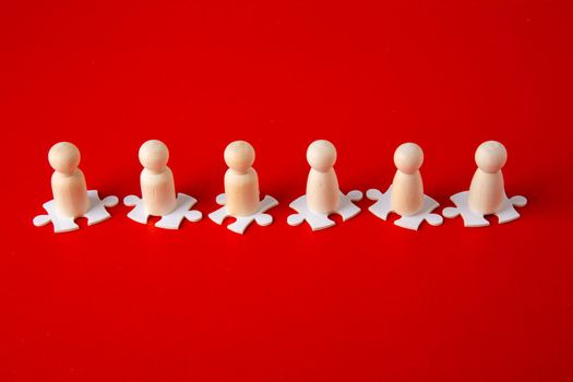 Wooden figures on puzzles on red background as a symbol of team building. Organization group people in business. Cooperation and partnership.