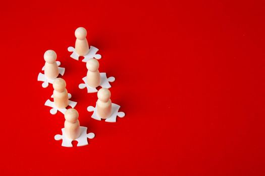 Wooden figures on puzzles on red background as a symbol of team building. Organization group people in business. Cooperation and partnership.