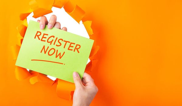hand holding green sheet with REGISTER NOW through hole in ripped orange paper. Business Concept