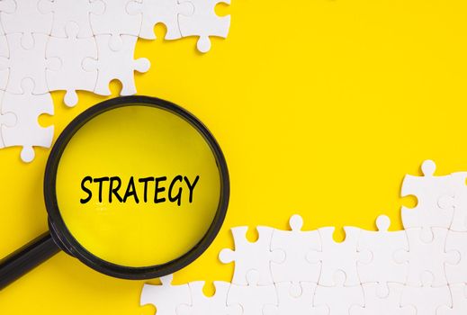 Top view of jigsaw puzzle and magnifying glass with Strategy word . Business concept.