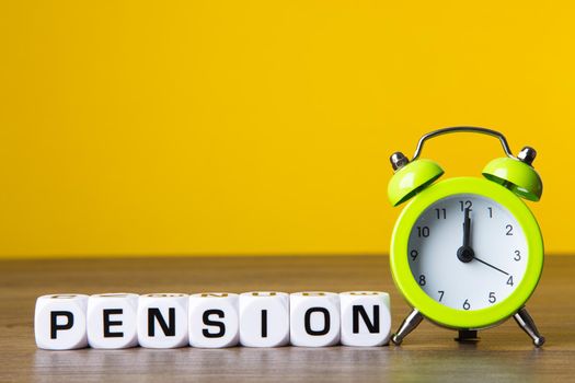 Inscription Pension and alarm clock on yellow background. Retirement Concept