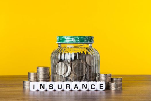 A lot coins in glass money jar with yellow background. Saving for Insurance concept.