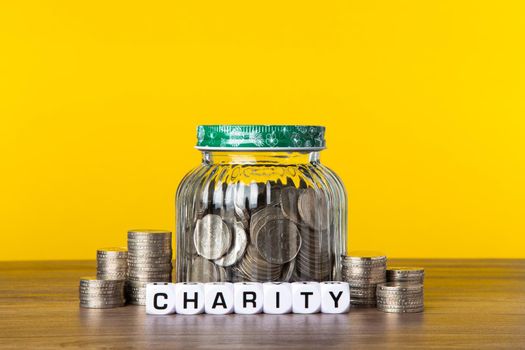 A lot coins in glass money jar with yellow background. Saving for Charity concept.
