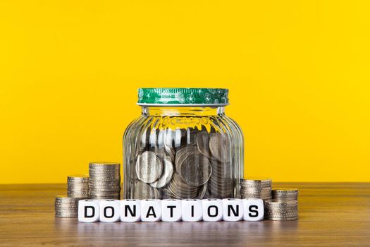A lot coins in glass money jar with yellow background. Saving for Donations concept.