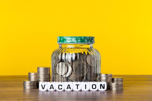 A lot coins in glass money jar with yellow background. Saving for Vacation concept.