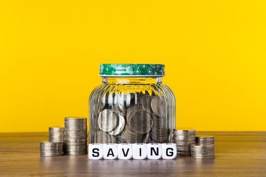 A lot coins in glass money jar with yellow background. Saving for Investment concept.