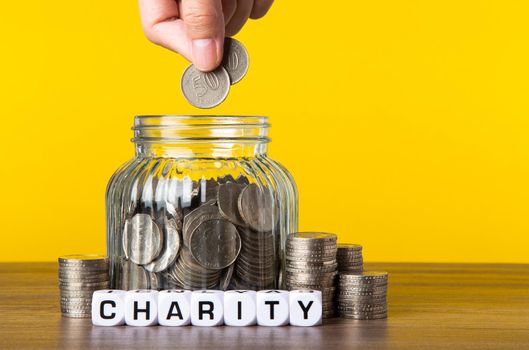 A lot coins in glass money jar with yellow background. Saving for Charity concept.