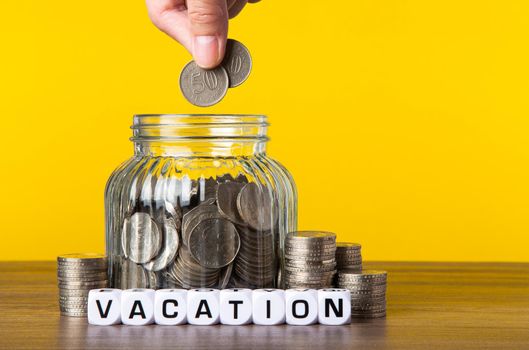 A lot coins in glass money jar with yellow background. Saving for Vacation concept.