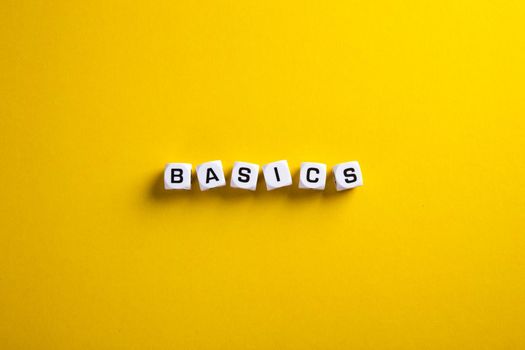 Basics word written on blocks on yellow background with flat lay view. Back to basics or simplifying business concept.