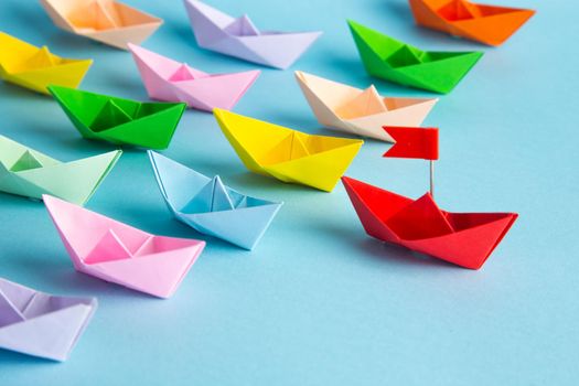 Leadership concept. Red leader paper ship leading among others on blue background.