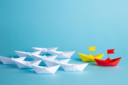 Leadership concept. Red leader paper ship leading among others on blue background.