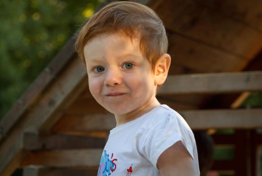 Portrait of a cute, redhead, blue-eyed boy wearing a white t-shirt in a playground on a sunny day