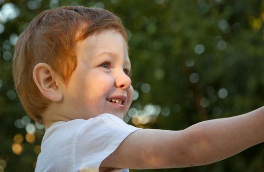 Portrait of a cute, redhead, blue-eyed boy wearing a white t-shirt in a playground on a sunny day