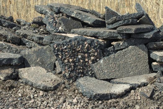 The asphalt pavement removed from the road lies in large chunks on the side of the road. Preparation for road repairs.