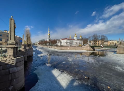 Russia, St. Petersburg, 01 April 2021: St. Nicholas Naval Cathedral belltower in a clear sunny day of spring, an ice drift on Kryukov and Griboyedov Canal, a view of seven bridges from the embankment. High quality photo