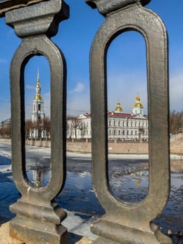 St. Nicholas Naval Cathedral belltower through the forged lattice in a clear sunny day of spring, an ice drift on Kryukov and Griboyedov Canal, a view of seven bridges from the embankment. High quality photo