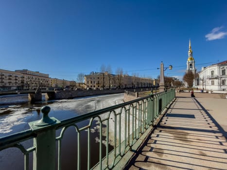 Russia, St. Petersburg, 01 April 2021: St. Nicholas Naval Cathedral belltower in a clear sunny day of spring, an ice drift on Kryukov and Griboyedov Canal, a view of seven bridges from the embankment. High quality photo