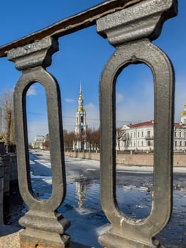 St. Nicholas Naval Cathedral belltower through the forged lattice in a clear sunny day of spring, an ice drift on Kryukov and Griboyedov Canal, a view of seven bridges from the embankment. High quality photo