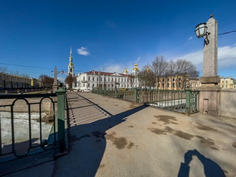 Russia, St. Petersburg, 01 April 2021: St. Nicholas Naval Cathedral belltower in a clear sunny day of spring, an ice drift on Kryukov and Griboyedov Canal, a view of seven bridges from the embankment. High quality photo