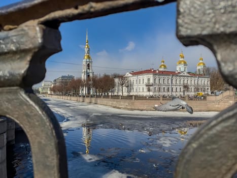 St. Nicholas Naval Cathedral belltower through the forged lattice in a clear sunny day of spring, an ice drift on Kryukov and Griboyedov Canal, a view of seven bridges from the embankment. High quality photo