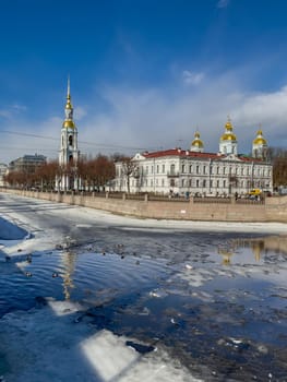 Russia, St. Petersburg, 01 April 2021: St. Nicholas Naval Cathedral belltower in a clear sunny day of spring, an ice drift on Kryukov and Griboyedov Canal, a view of seven bridges from the embankment. High quality photo