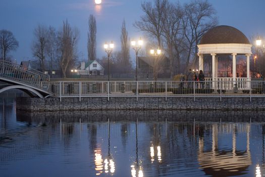 Gazebo on an artificial lake at night. Reflection in the water of the gazebo and the glowing lanterns. Ukraine, Kremenchug