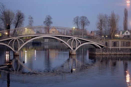 Bridge on an artificial lake in a city park at night. Reflection of the bridge from the water. Kremenchug, Ukraine.