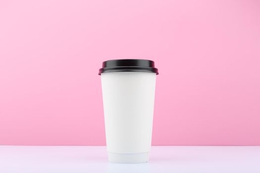 White tall disposable cup for tea or coffee on white table against bright purple background with copy space. Concept of disposable cups and hot drinks