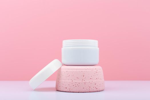 White opened cosmetic jar on pink podium against bright pink background. Face creme, mask or scrub for skin care and beauty or anti aging treatment