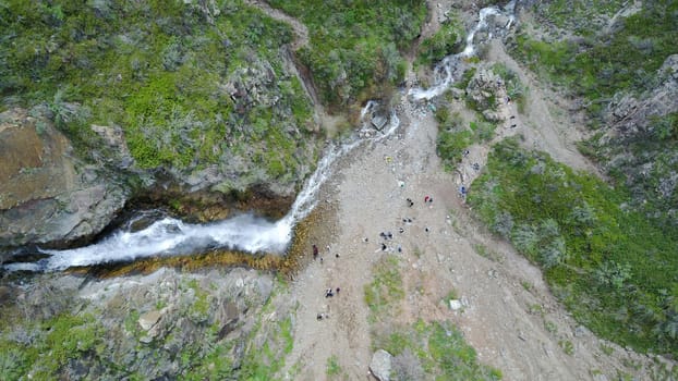 Top view of the waterfall among the rocks. Highest waterfall, and longest river. Grass and trees grow on the rock. A group of people can be seen below. Outdoor recreation. Mountainous area.