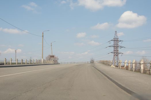 Paved road across the bridge. High-voltage power transmission tower. Against the blue sky on a sunny day. no cars. elevated road