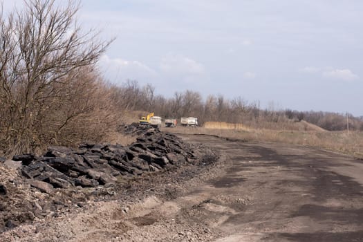 Road before repair. The removed asphalt is lying on the side of the road. Construction equipment in the distance.