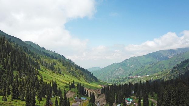 Green gorge with forest in the mountains. Aerial view of green hills, coniferous trees, road, river and trail. Steep cliffs with large rocks. The gorge is foggy, dripping rain in places. Kazakhstan.