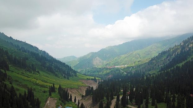 Green gorge with forest in the mountains. Aerial view of green hills, coniferous trees, road, river and trail. Steep cliffs with large rocks. The gorge is foggy, dripping rain in places. Kazakhstan.