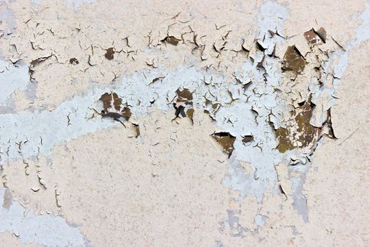 Light coloured paint peels and cracks off of a metal surface showing a brown colour beneath. The paint is heavily cracked and weathered.