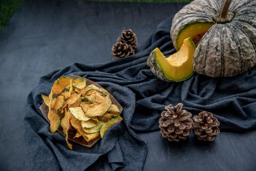 Flat Lay composition with delicious of Homemade crispy pumpkin chips on Black stone texture. Oblique view from the top.