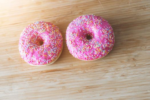 Sugar sprinkled pink donut on wooden plate