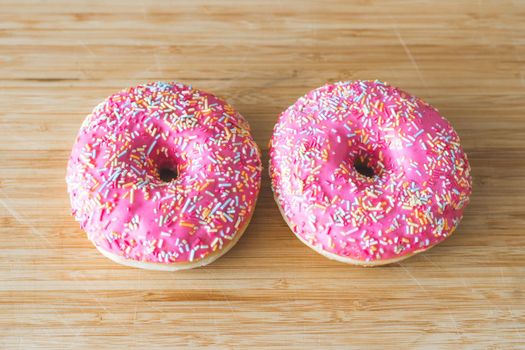 Sugar sprinkled pink donut on wooden plate