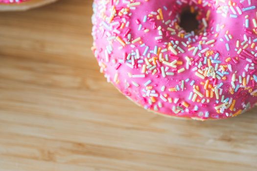 Sugar sprinkled pink donut on wooden plate