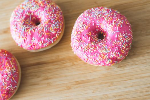 Sugar sprinkled pink donut on wooden plate