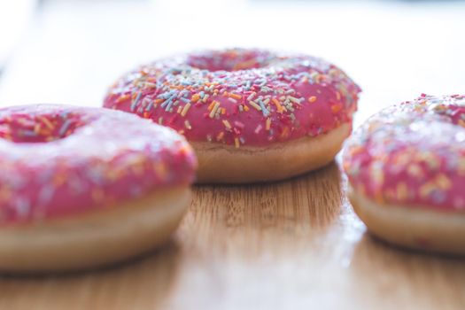 Sugar sprinkled pink donut on wooden plate