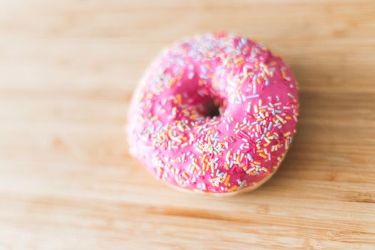 Sugar sprinkled pink donut on wooden plate