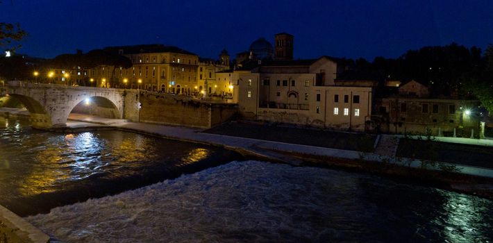 A view of the Tiberine Island at night with Tiber river flowing in the foreground