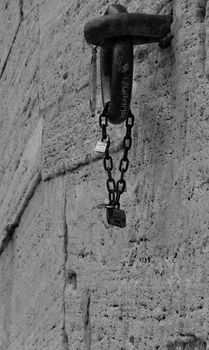 Detail of a chain locked with padlocks hanging from an iron ring in a stone wall