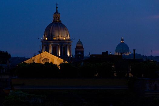 Lighted domes and roofs of Rome at dusk against a dark blue sky