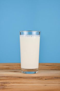 Close up one glass full of fresh milk on wooden table over blue background, low angle, side view