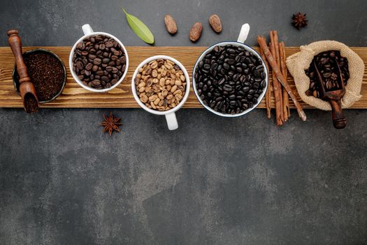 Brown unroasted and dark roasted coffee beans in coffee cup with scoops setup on dark stone background.