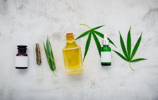 Glass bottle of cannabis oil and hemp leaves set up  on concrete background.