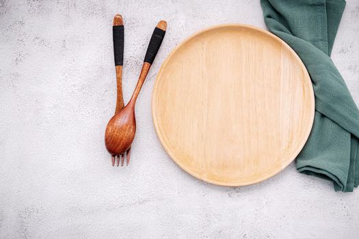 Empty wooden plate and green linen napkin with wooden spoon on white concrete  background .