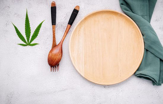 Food conceptual image of a cannabis leaf  with spoon and fork on white concrete background.